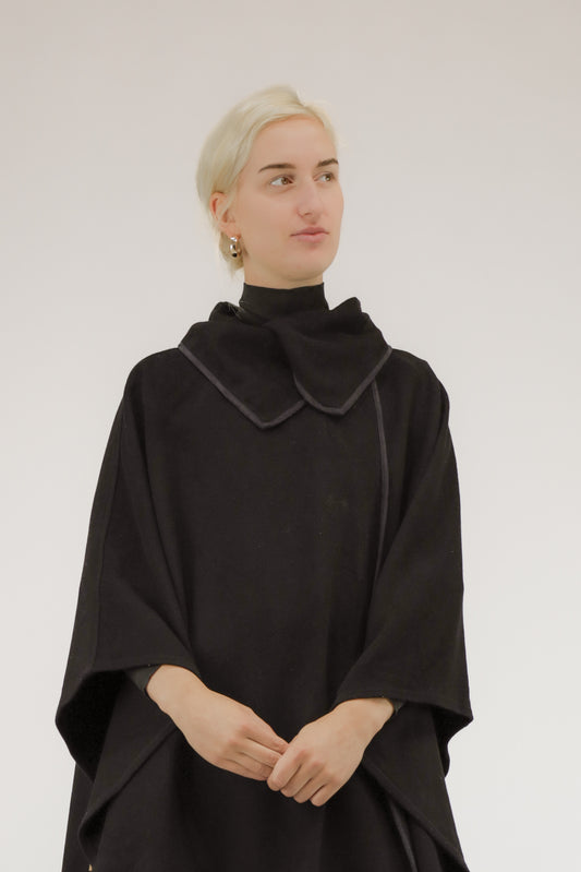 Detailopname van zwarte poncho, close-up van biasband en wolstructuur.